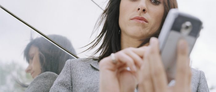 Business woman standing outside in front of office building, using mobile phone --- Image by © Royalty-Free/Corbis